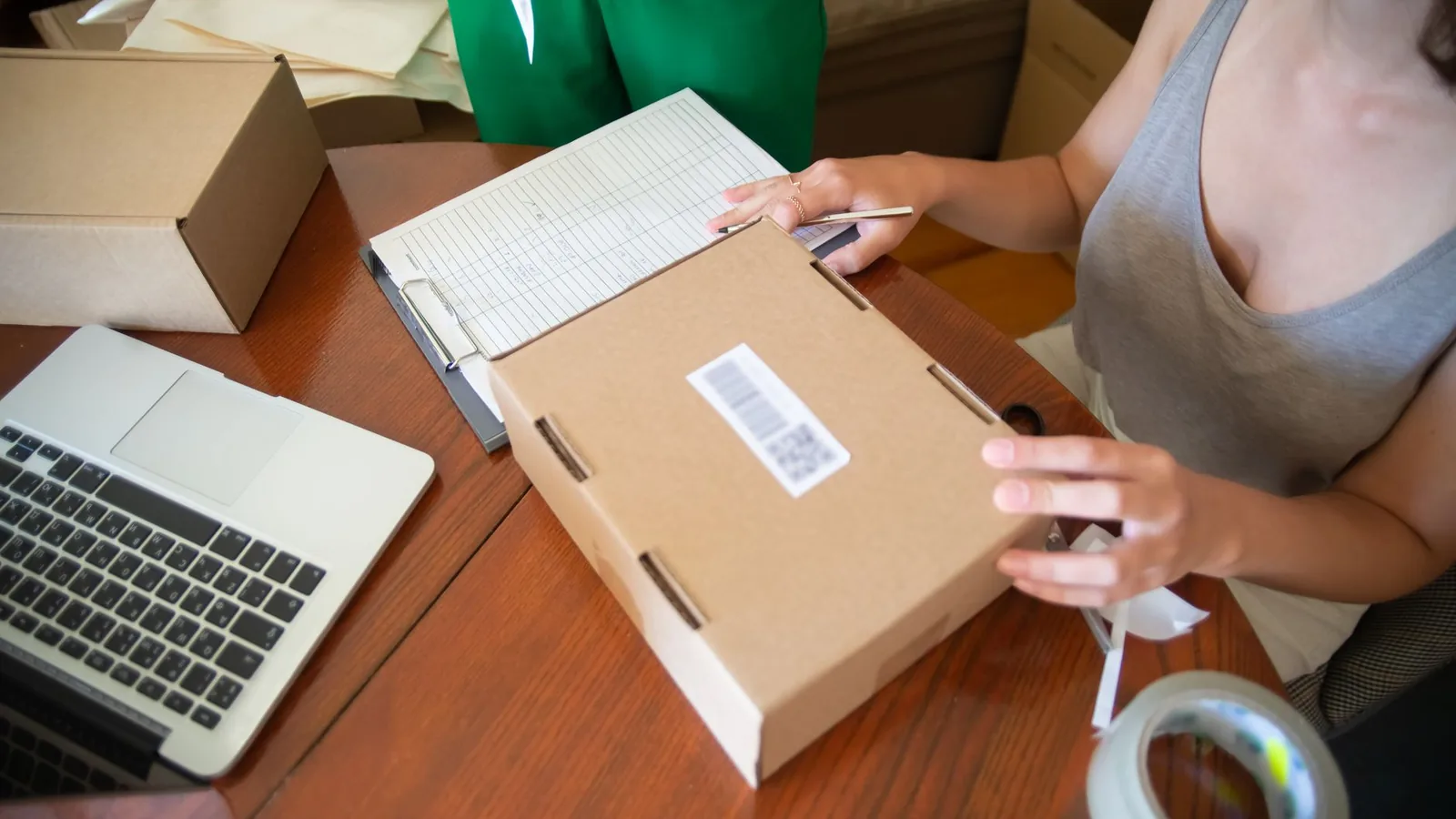 Dueña de un negocio revisando pedidos en línea desde su celular junto a cajas listas para enviar